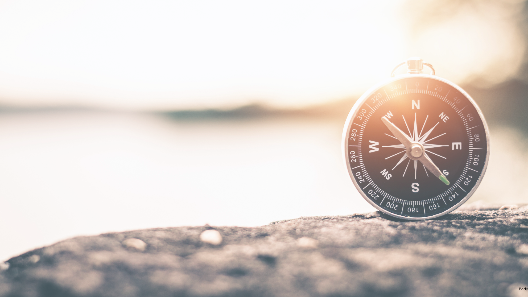 A compass on a rock overlooking the water, symbolizing the one-degree shift founders need to reduce overwhelm and realign their leadership trajectory.